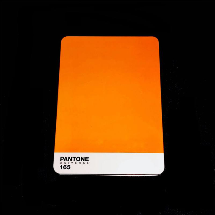 Eine orange Farbkarte mit der Aufschrift Pantone Universe 165. Sie liegt auf einem schwarzen Hintergrund.
