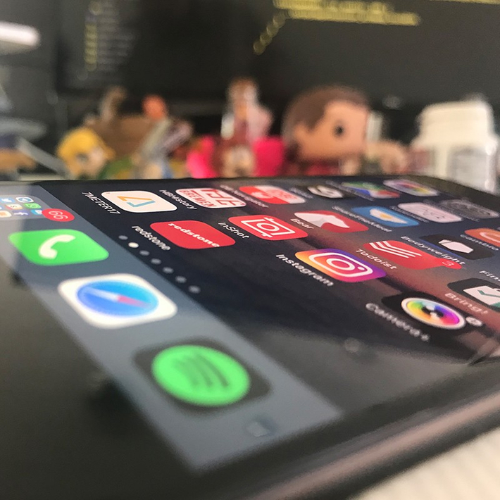 Ein Smartphone angewinkelt liegend, vor verschiedenen Figuren und einem Computer-Bildschirm.
