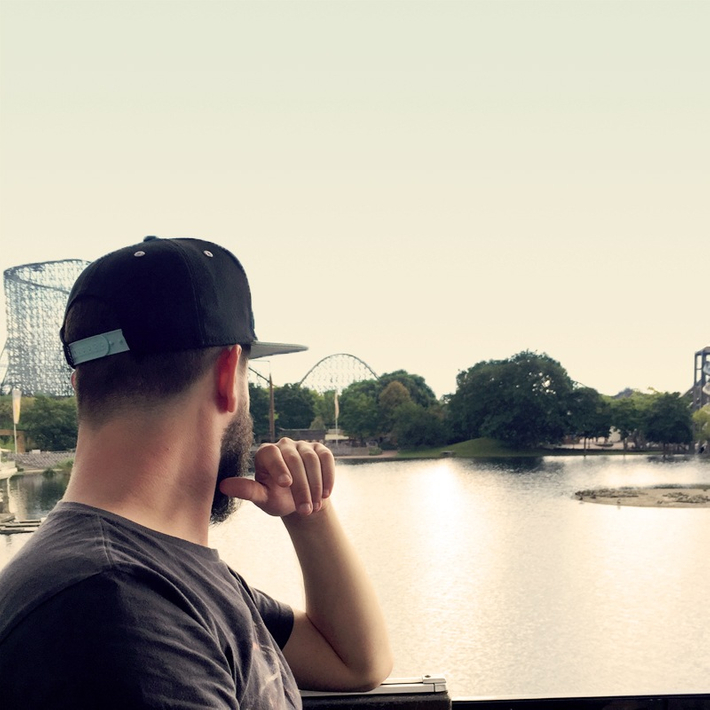 Kevin mit Blick auf einen See. Am Ende des Sees sind Bäume und eine Achterbahn zu sehen.