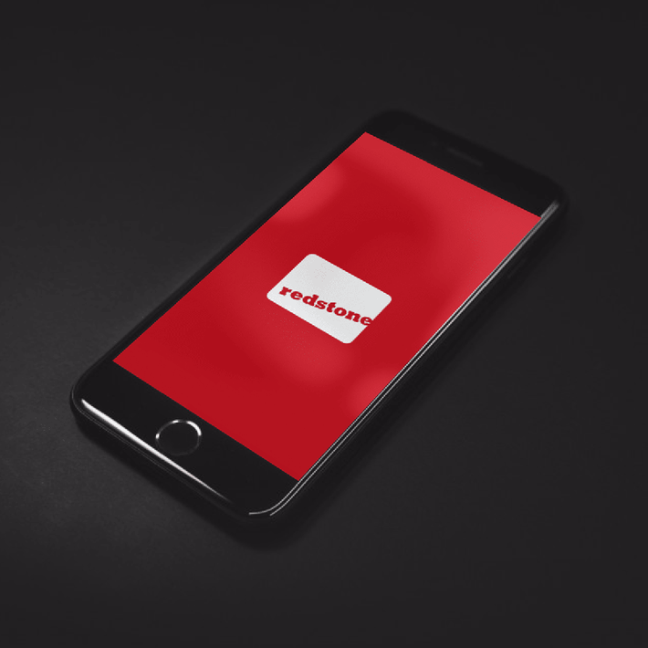 Ein iPhone, auf dem die Bildmarke des redstone-Logos auf rotem Hintergrund zu sehen ist. Das iPhone befindet sich vor einem schwarzen Hintergrund.
